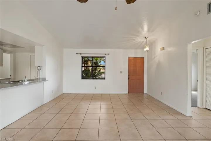 Unfurnished living room with an inviting chandelier, light tile patterned floors, vaulted ceiling, and sink