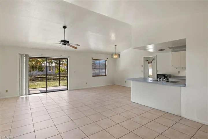 Unfurnished living room with lofted ceiling, sink, ceiling fan with notable chandelier, and light tile patterned floors