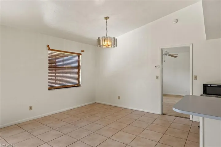 Unfurnished dining area with light tile patterned floors and ceiling fan with notable chandelier