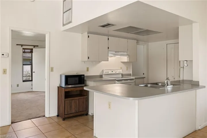 Kitchen featuring white electric range, sink, white cabinetry, light tile patterned floors, and kitchen peninsula