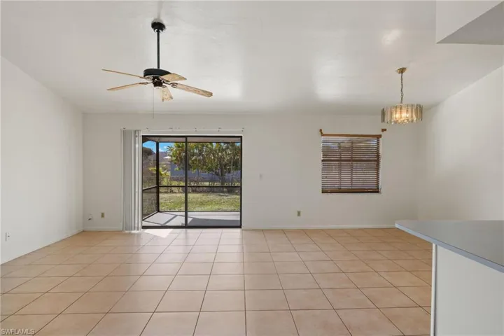 Tiled spare room featuring ceiling fan with notable chandelier