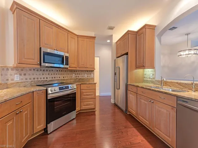 Kitchen with stainless steel appliances, granite countertops, dark wood-style floors, Marble backsplash, and a chandelier