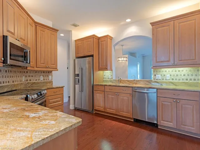 Kitchen with stainless steel appliances, granite countertops, dark wood-style floors, Marble backsplash, and a chandelier