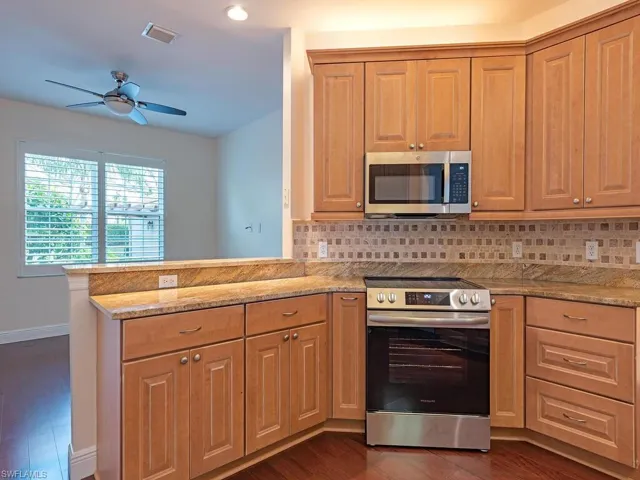 Kitchen with stainless steel appliances, granite countertops, dark wood-style floors, Marble backsplash, and a chandelier