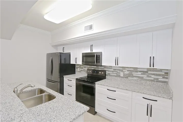 Kitchen featuring ornamental molding, stainless steel appliances, white cabinetry, tasteful backsplash, and light stone counters