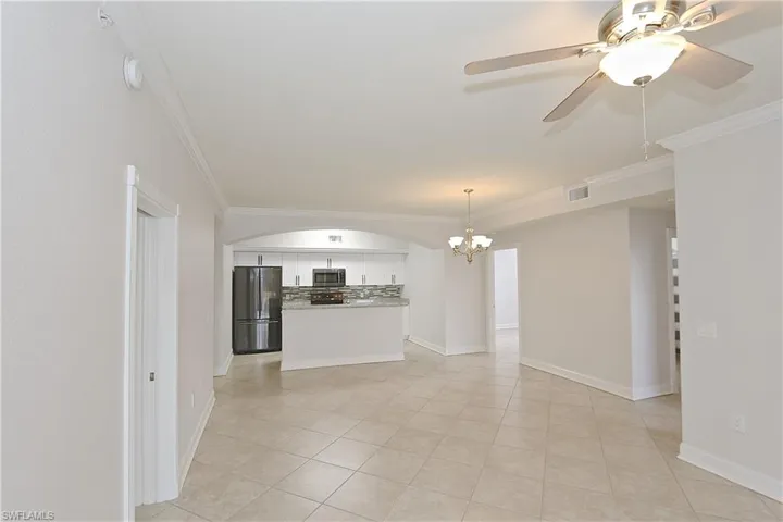 Unfurnished living room with a chandelier, ornamental molding, a ceiling fan, light tile patterned flooring, and arched walkways