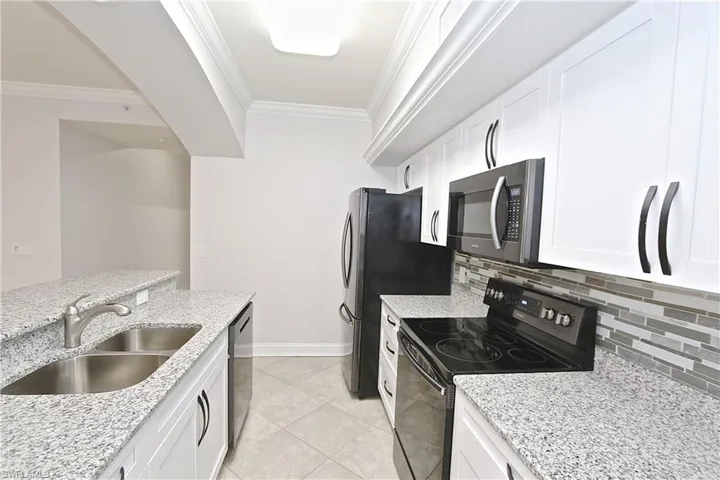 Kitchen with black range with electric cooktop, ornamental molding, backsplash, and white cabinets