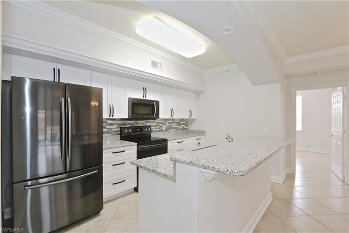 Kitchen featuring stainless steel appliances, ornamental molding, decorative backsplash, light tile patterned flooring, and white cabinets