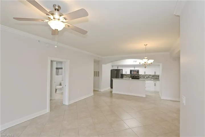 Unfurnished living room with crown molding, a chandelier, ceiling fan, light tile patterned floors, and arched walkways