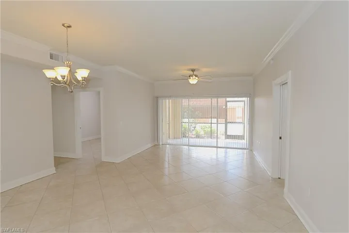 Empty room with crown molding, ceiling fan, light tile patterned floors, and a chandelier