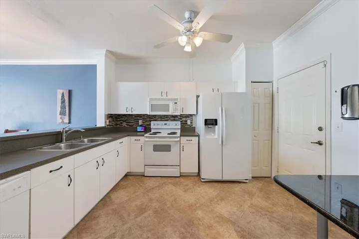 Kitchen featuring white appliances, ceiling fan, a sink, crown molding, and dark countertops