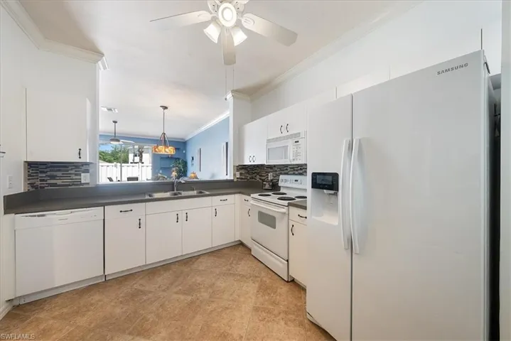 Kitchen featuring white appliances, a sink, crown molding, dark countertops, and tasteful backsplash