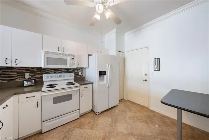 Kitchen with backsplash, dark countertops, ornamental molding, and white appliances
