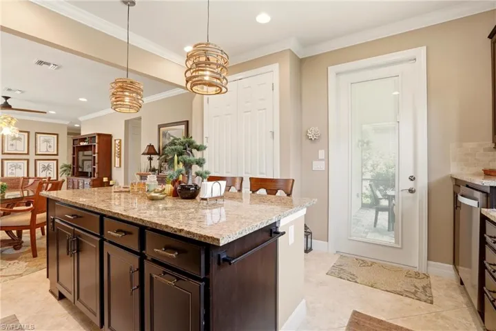 Kitchen featuring dark wood finish cabinetry, light granite counters, crown molding, decorative light fixtures, and a center island