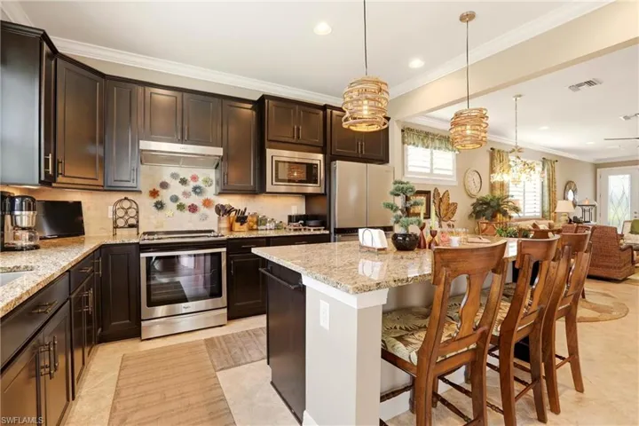 Kitchen featuring light granite countertops, dark wood finish cabinetry, decorative backsplash, a breakfast bar, and crown molding