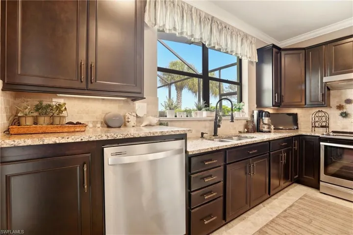 Kitchen with tasteful backsplash, stainless steel appliances, dark wood finish cabinetry, light granite countertops, and ornamental molding