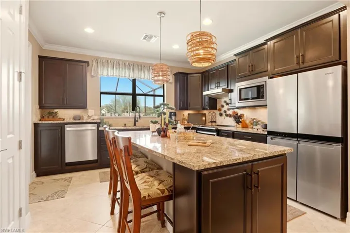 A Chef's kitchen with dark wood finish cabinetry, stainless steel appliances, a kitchen island, light granite countertops, and a breakfast bar