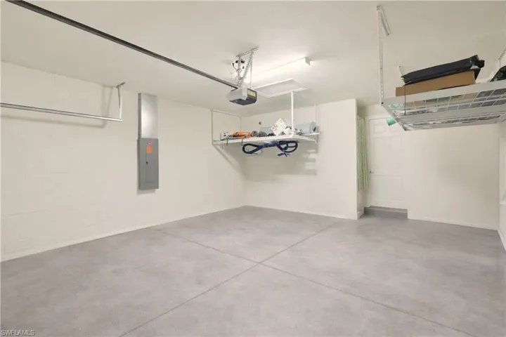 Garage with electric panel, concrete block wall, and a garage door opener.  Notice the suspended storage shelving.