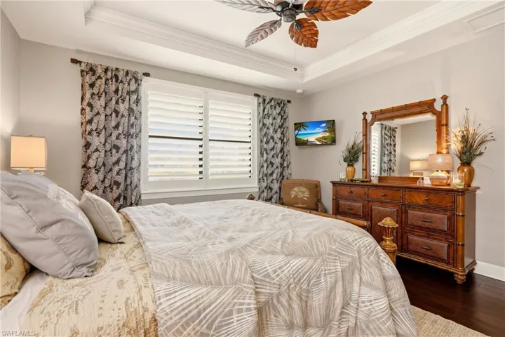 Primary Bedroom featuring crown molding in the Tray area, a raised ceiling, hardwood laminate flooring, and a ceiling fan