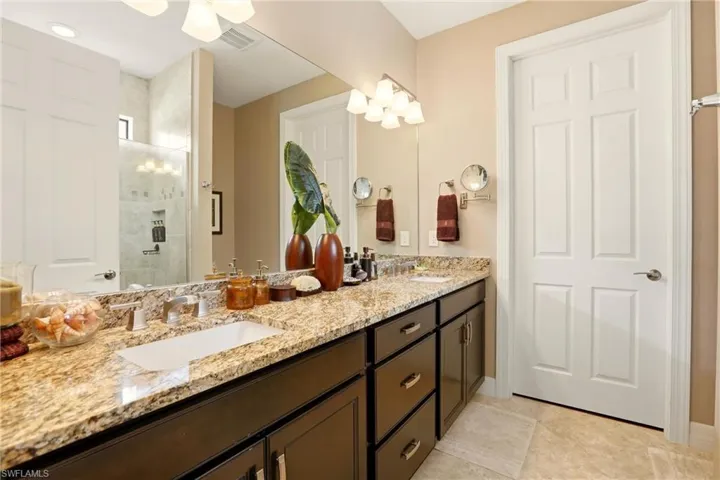 Primary Bathroom with double vanity, granite countertops and light tile patterned flooring