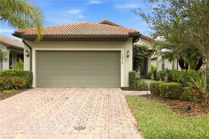 View of front of property with a tiled roof, stucco siding, an attached garage, and brick paver driveway