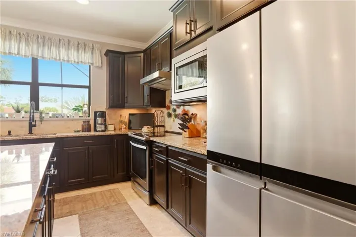 Kitchen featuring stainless steel appliances, dark wood finish cabinetry, crown molding, light granite countertops, and tasteful backsplash