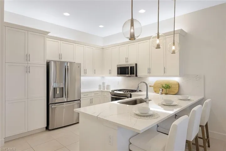 Kitchen with kitchen peninsula, backsplash, hanging light fixtures, appliances with stainless steel finishes, and a breakfast bar