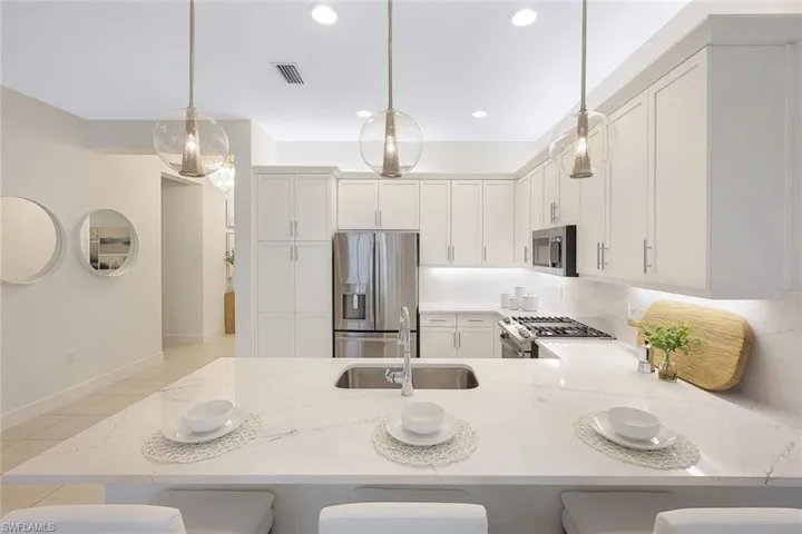 Kitchen featuring a kitchen breakfast bar, appliances with stainless steel finishes, kitchen peninsula, decorative light fixtures, and sink