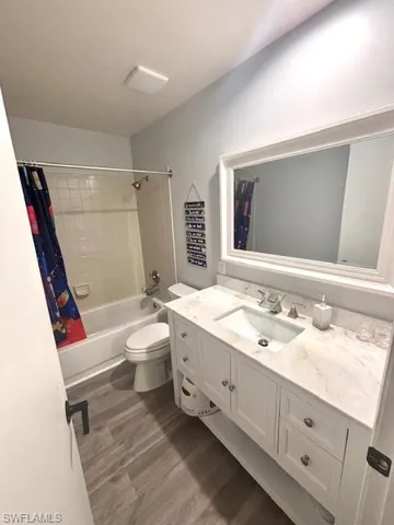 Full bath featuring shower / bath combination with curtain, vanity, and dark wood-style flooring