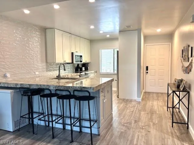 Kitchen featuring a breakfast bar area, light stone countertops, decorative backsplash, recessed lighting, and light wood finished floors