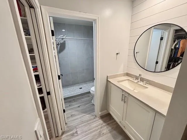 Bathroom featuring a walk in closet, vanity, a stall shower, and light wood-style flooring