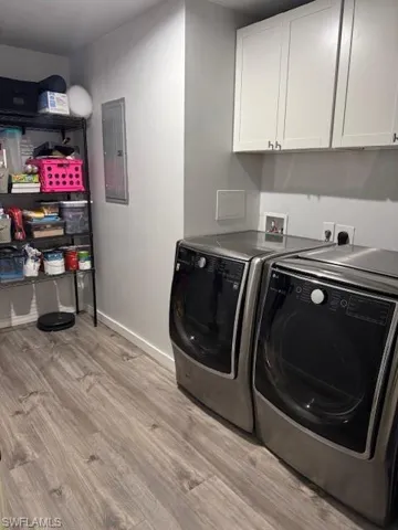 Laundry room with light wood finished floors, cabinet space, electric panel, and washing machine and clothes dryer