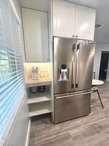 Kitchen with stainless steel refrigerator with ice dispenser, dark wood-style flooring, backsplash, and white cabinetry