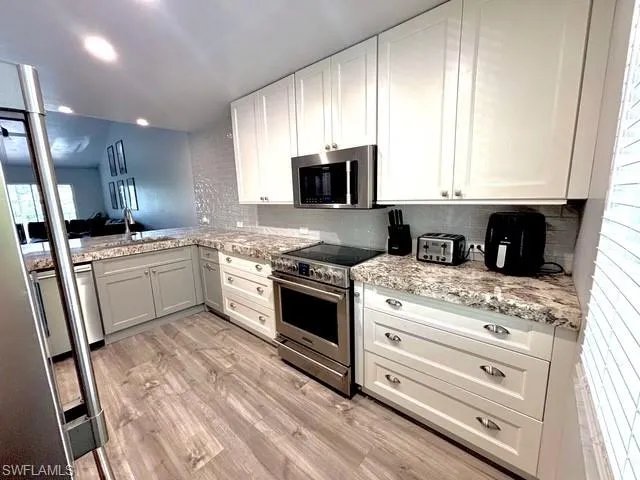 Kitchen featuring stainless steel appliances, light stone counters, light wood-style floors, white cabinets, and backsplash