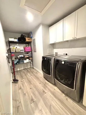 Laundry area with light wood-style flooring, cabinet space, washing machine and dryer, and electric panel