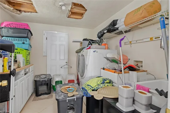 Laundry area with washer / dryer, a textured ceiling, and light tile floors