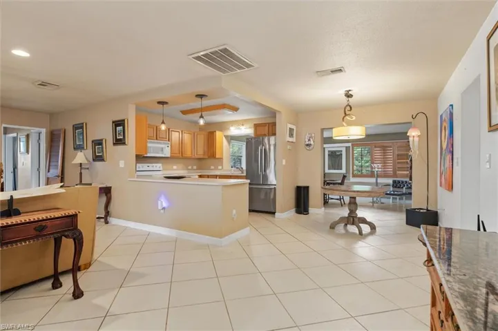 Kitchen with hanging light fixtures, a raised ceiling, light tile flooring, and white appliances
