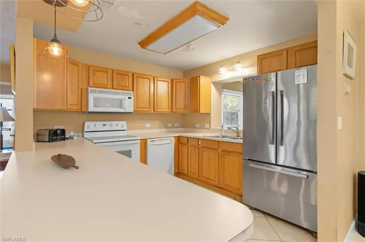 Kitchen with sink, white appliances, pendant lighting, and light tile floors
