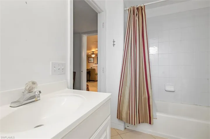 Bathroom with shower / bathtub combination with curtain, tile flooring, and oversized vanity