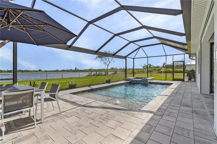 View of swimming pool featuring a water view, a lanai, a yard, an in ground hot tub, and a patio