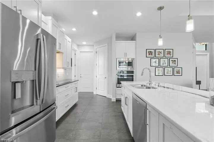 Kitchen featuring a center island with sink, wine fridge, hanging light fixtures, appliances with stainless steel finishes, tasteful backsplash, and white cabinetry