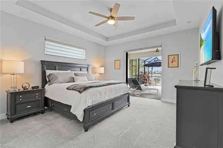Master bedroom featuring access to exterior, light carpet, a tray ceiling, and ceiling fan