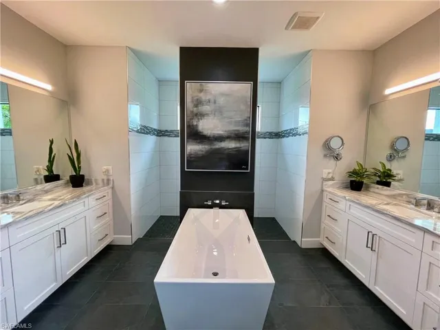 Master bathroom with dual vanities, freestanding tub, and walkaround shower