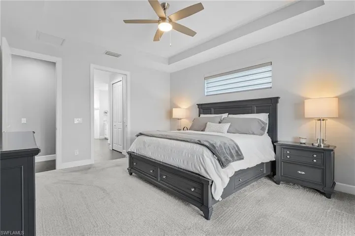 Master bedroom with light carpet, ensuite bath, and ceiling fan