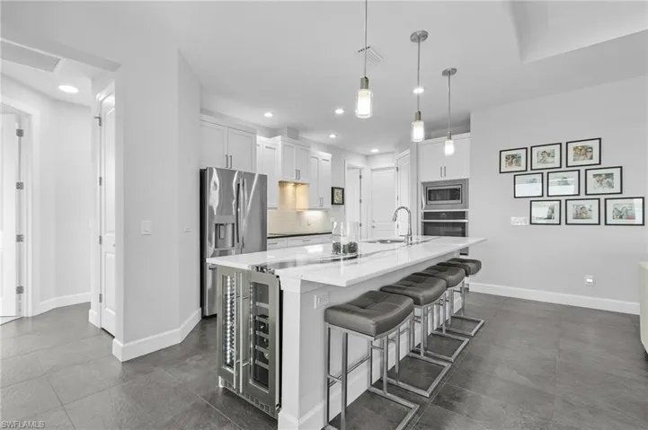 Kitchen featuring a center island with sink, wine fridge, hanging light fixtures, appliances with stainless steel finishes, tasteful backsplash, and white cabinetry