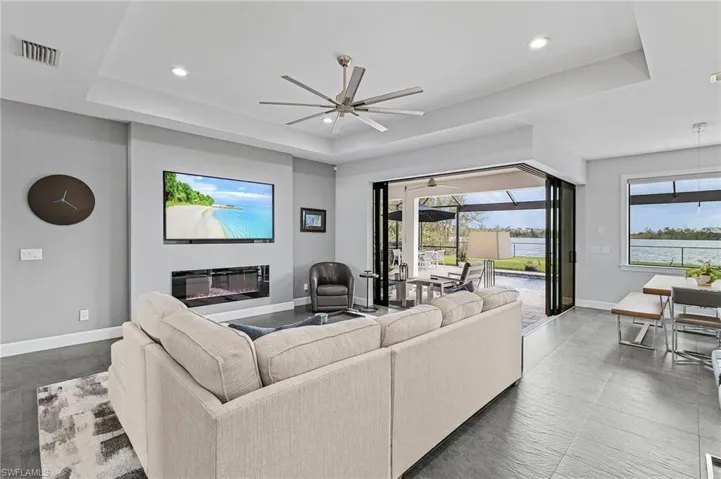 Living room with a tray ceiling, a wealth of natural light, electric fireplace, and ceiling fan