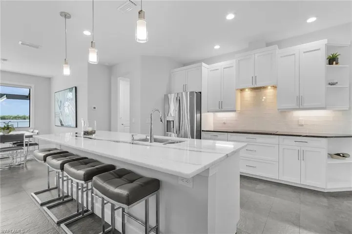 Kitchen with stainless steel fridge, sink, decorative light fixtures, a center island with sink, and white cabinets