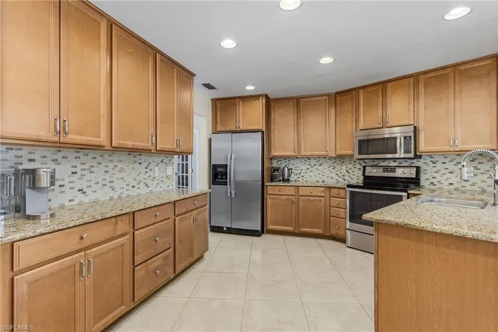 Kitchen with light stone counters, light tile patterned flooring, sink, backsplash, and appliances with stainless steel finishes