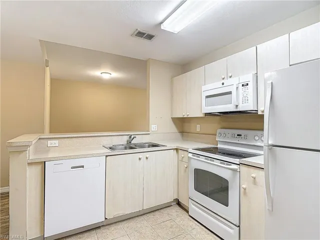 Kitchen with sink, kitchen peninsula, white appliances, and light tile floors