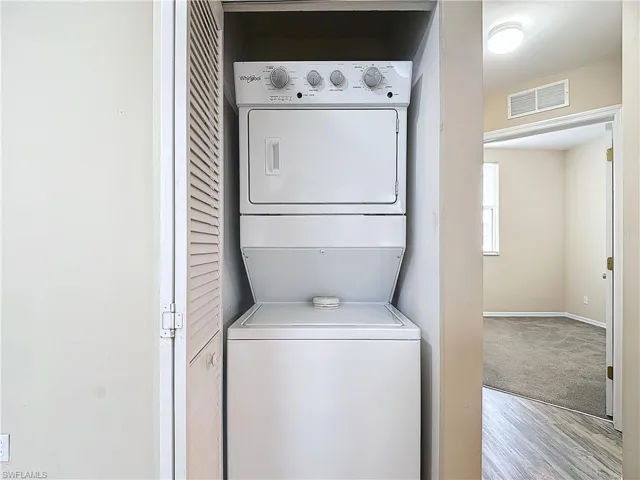 Laundry area with stacked washing maching and dryer and light colored carpet